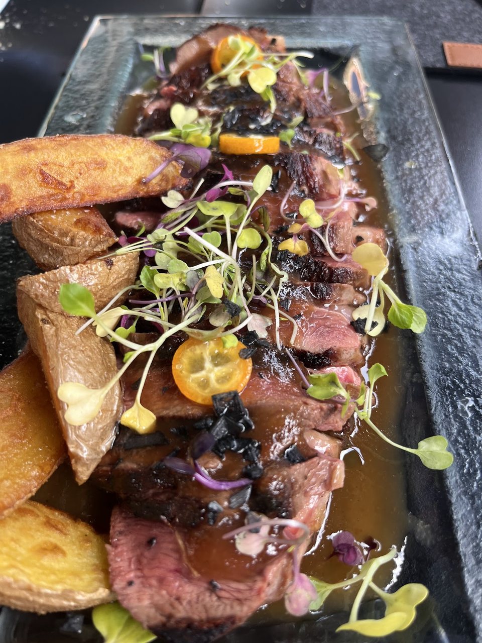Plato de entrecot laminado con patatas rústicas y kumquat, cocina de mercado.